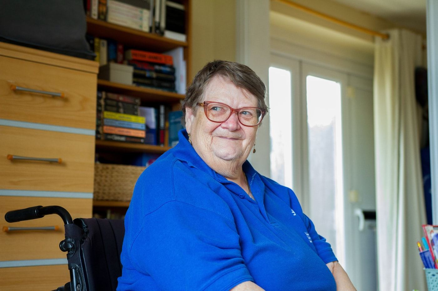 A smiling woman sits in her wheelchair at home